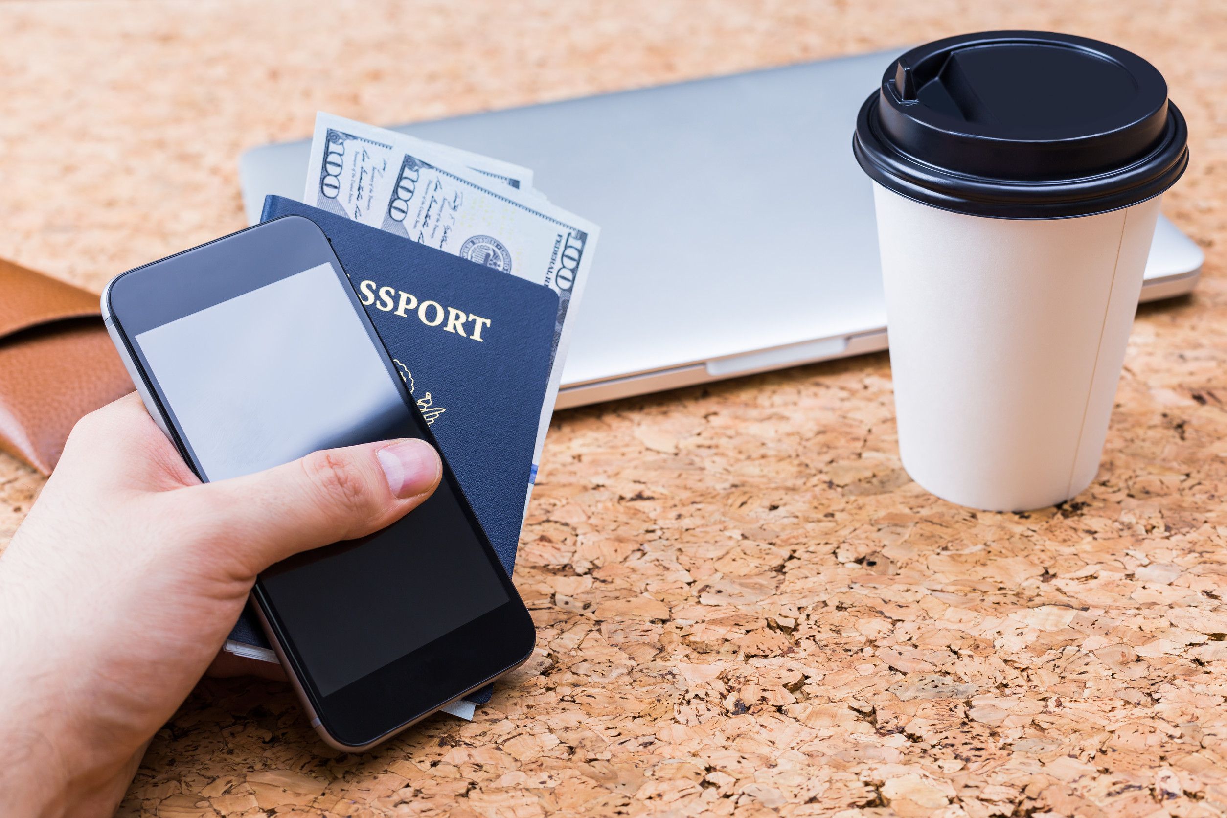 Cork Table With Closed Laptop Coffee Cup And Hand Holding Smartphone